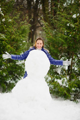 White Christmas. Cute young woman builds a big snowman in the park.