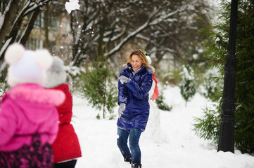 Fototapeta premium White Christmas. Girl plays with mother in snowballs in the winter park.