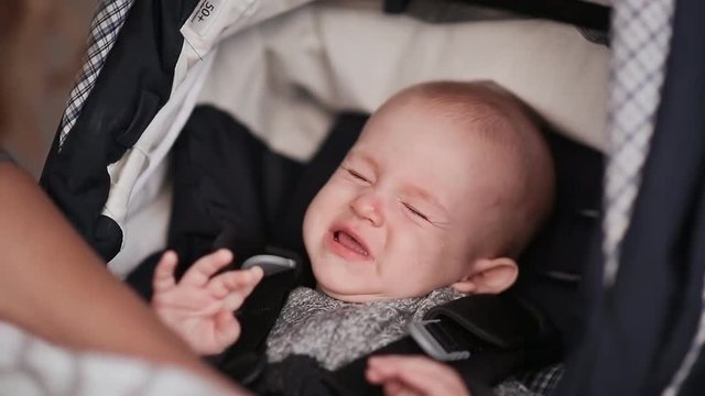 Little baby boy in stroller outdoors. Baby wakes up.