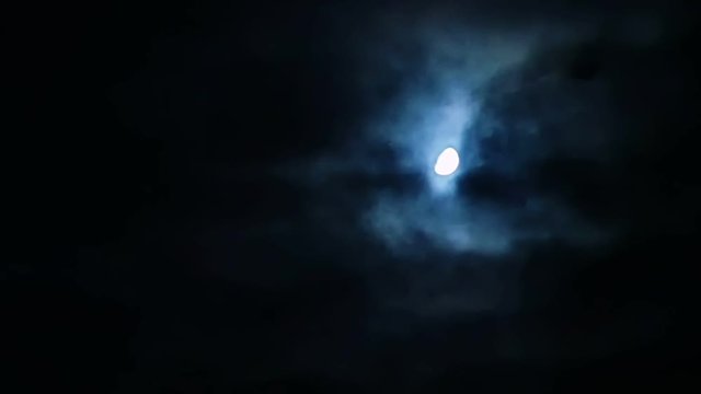 Storm clouds moving over the moon at night on overcast dark sky. Windy bad weather and horror scene.