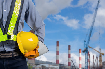 Engineer holding yellow helmet with coal power plant.