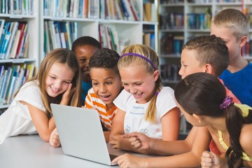 Smiling school kids looking at laptop in library