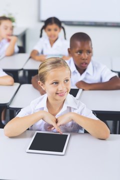 Smiling schoolgirl using digital tablet in classroom