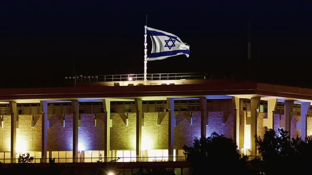 Knesset building the Parliament of Israel with flying waving flag of Israel at night. The knesset located in Jerusalem and elects both President and Prime Minister and supervises Israeli government
