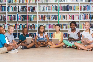 School kids sitting on floor using digital tablet in library