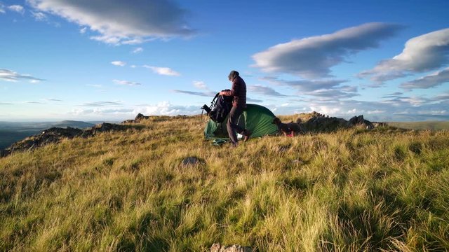 A hiker returning to their tent with their dog on the summit of Place Fell in the English Lake District in the UK.