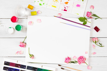 Sketchbooks, brushes, watercolor paints, palette and pink roses.