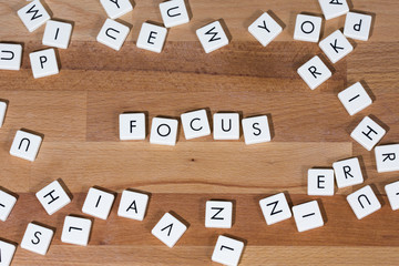 Focus text on a wooden surface. The text is surrounded by letters to emphasise the concentration.