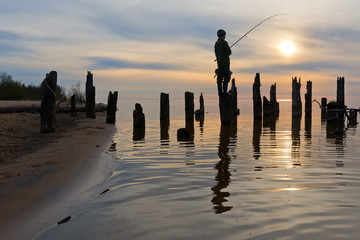 Silhouette of boy on pole of pier catching fish.
