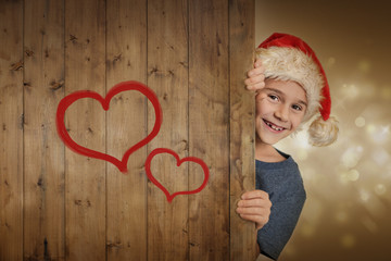 Lachender Junge mit Weihnachtsmütze hinter Holzwand