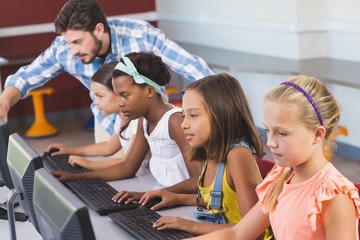 Teacher assisting schoolgirls in learning computer