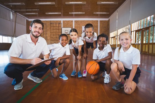 Portrait of sports teacher and school mixed race kids in basketball court
