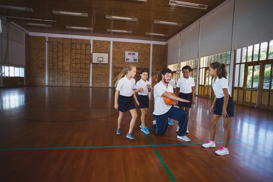 Sports teacher teaching school kids to play basketball