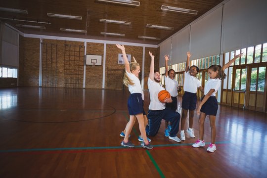 Sports teacher and school kids playing in basketball court