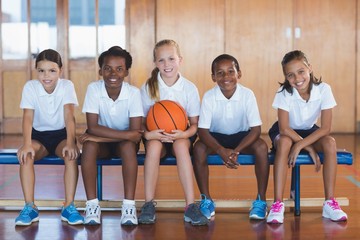 Portrait of school kids sitting in basketball court
