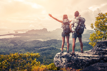 Hikers with backpacks relaxing on top of a mountain and enjoying the view of valley