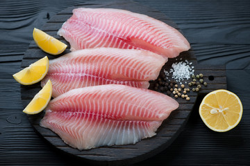 Black wooden chopping board with raw fresh tilapia fillets