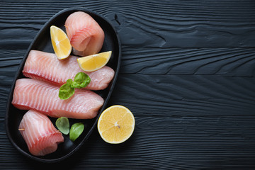 Marinated tilapia filet over black wooden surface with copyspace