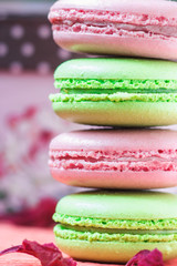 Stacked, tasty pink and green Macaroons, colorful delicious French pastries, strawberry and pistachio macaroons decorated with dry peony petals on pink paper background.