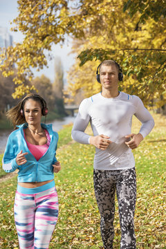 Beautiful young couple listening music and running together in the park. Autumn environment.