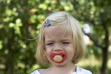 Profile portrait of little child blond girl with dummy outdoors

