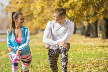 Beautiful young couple stretching together and preparing for run in the park. Autumn environment.