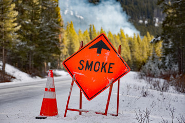 smoke ahead sign in the winter with a small plume of smoke in background
