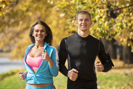 Beautiful young couple running together in the park. Autumn environment.