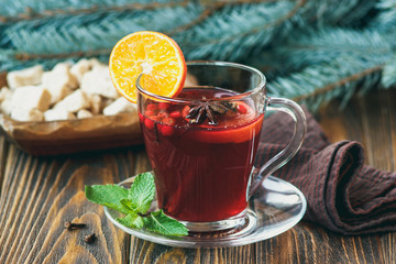 Hot red mulled wine on wooden background decorated blue spruce branches, with christmas spices, orange slice, fresh mint, cloves, anise and cinnamon sticks, close up.