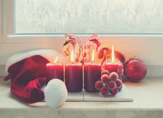 Christmas scene with four red burning candles on frozen windowsill, retro toned