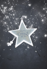 Merry Christmas star on black wooden background with snow