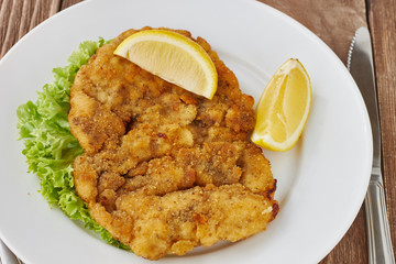 Weiner schnitzel with green salad and lemon on a wooden background