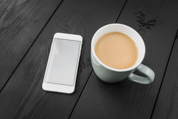 Cup of coffee and smart phone with white screen on the black wooden background.