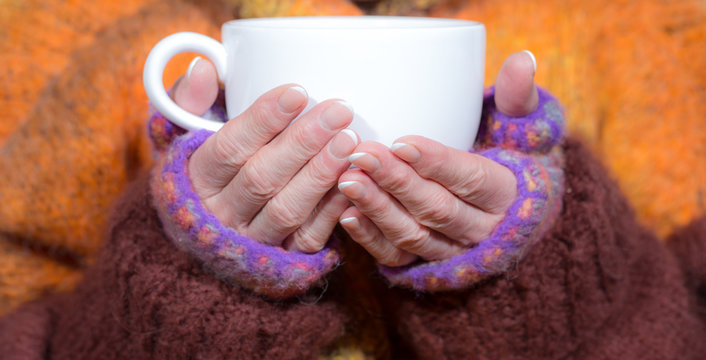 A woman is warming her fingers on a hot cup of tea