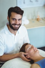 Smiling physiotherapist giving head massage to a woman