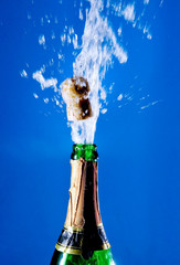 Bottle of champagne with a popping cork (against a bright blue background)
