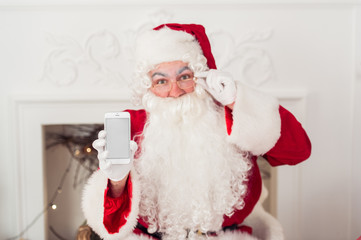 Santa Claus shows a smartphone against fireplace
