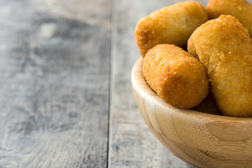 Traditional fried Spanish croquetas (croquettes) in bowl on wooden background
