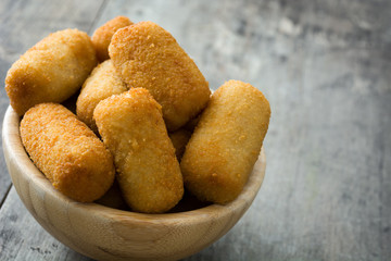 Traditional fried Spanish croquetas (croquettes) in bowl on wooden background
