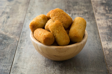 Traditional fried Spanish croquetas (croquettes) in bowl on wooden background
