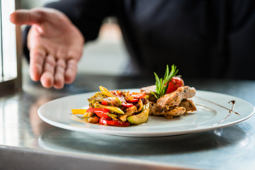 Koch zeigt stolz das von ihm gekochte Essen oder Gericht auf Anrichte in Restaurant Küche