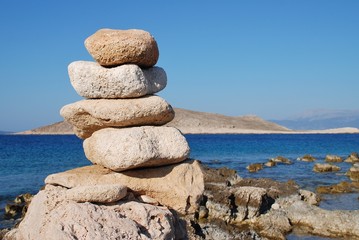 A tower of stones on Ftenagia beach at Emborio on the Greek island of Halki. The uninhabited island of Nissos is in the background.