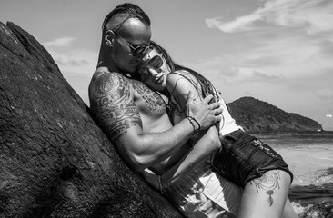 Attractive young topless couple hugging while leaning against the rock by the sea over sky...