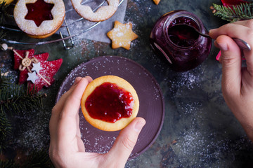 Process making of cookies by hand. Christmas Linzer cookies with raspberry jam on green table background. Top view and copy space. Hands cooking