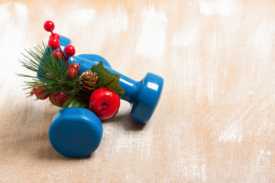 Christmas sport composition with dumbbells, red berries and spruce on plywood background. Concept Christmas special for healthy lifestyle and sport. 