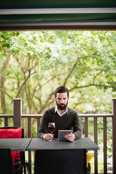 Man using digital tablet while having glass of wine