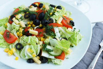 vegetable salad with corn, cheese and black olives in a white plate 
