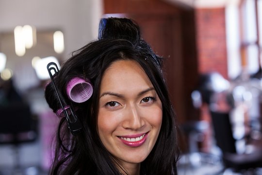 Smiling woman sitting with hair rollers at a salon