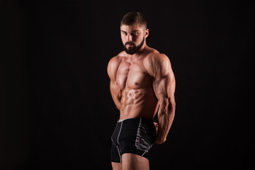 Fototapeta na wymiar Handsome muscular bodybuilder posing over black background.