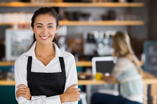 Portrait of smiling waitress standing with arms crossed